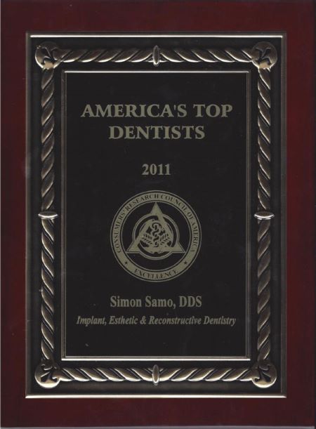 Wooden plaque with a metal plate for "AMERICA'S TOP DENTISTS 2011" presented to "Simon Samo, DDS" for "Implant, Esthetic & Reconstructive Dentistry" by the "CONSUMERS' RESEARCH COUNCIL OF AMERICA", featuring their circular "EXCELLENCE" logo.
