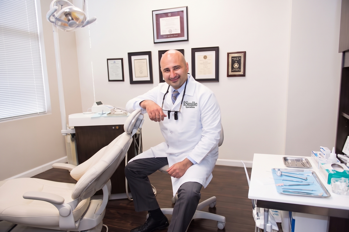 Prosthodontist Dr. Samo sitting in his dental exam room with his degress in the background. 
