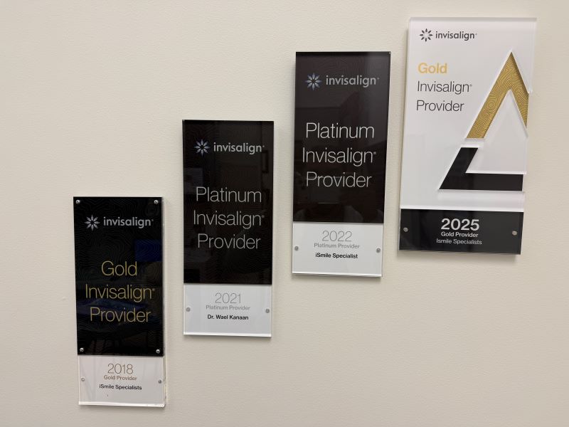 A collection of four Invisalign provider awards from iSmile Specialists and Dr. Wael Kanaan, showcasing the practice's achievements from 2018 to 2025. The awards are displayed on a light wall, featuring different provider statuses like Gold and Platinum.